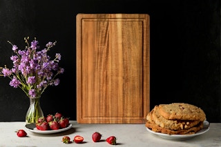 Lifestyle image of the Kikcoin Acacia Wood Cutting Board in a setting with strawberries and a plate of cookies