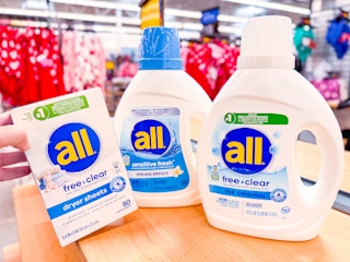 two bottles of all detergent and a hand holding dryer sheets on walmart counter