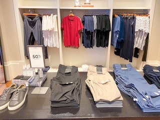 a display of pants on a table with a 50 percent off sale sign and pair of shoes in the mens section in banana republic