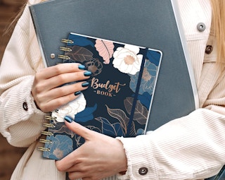 a person holding a notebook and floral planner in their arms