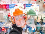 hand holding 2 dr brown's sippy cups in front of a target shelf