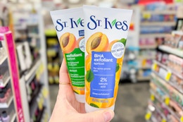 person holding 2 bottles of st ives face scrub
