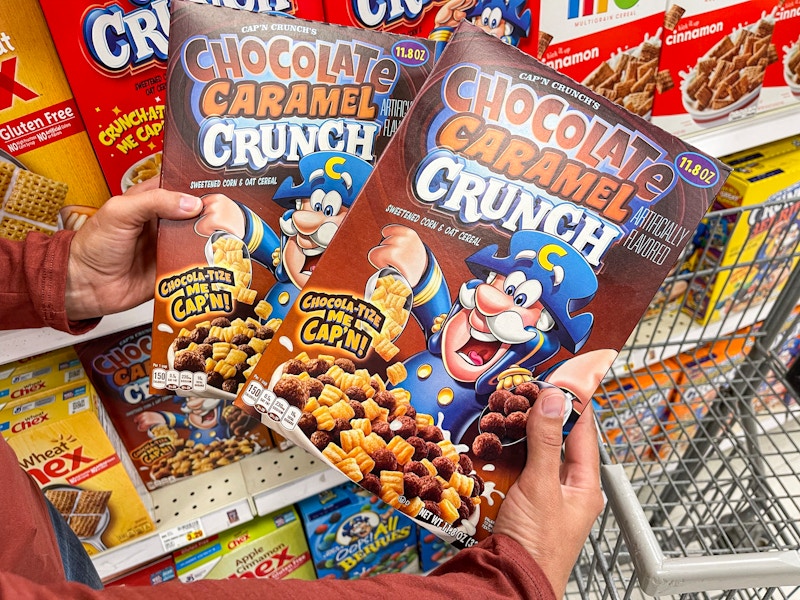 a person holding two boxes of capn crunch in store