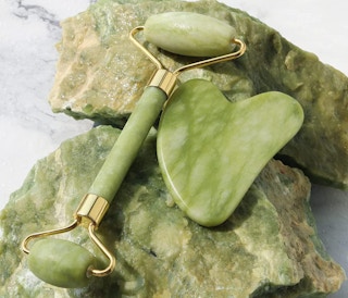 A Gua Sha and Jade Roller on green rocks
