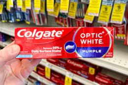 hand holding colgate toothpaste box in front of store shelves with sales tags