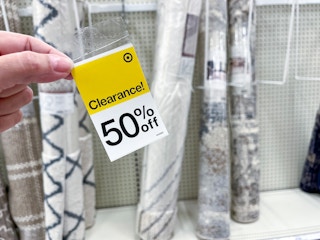 hand holding a target 50% off clearance tag in front of rugs