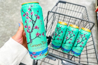 person holding a can of arizona tea over a cart with 3 more cans in it