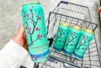 person holding a can of arizona tea over a cart with 3 more cans in it