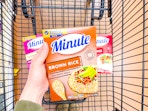 hand holding a box of minute rice over shopping cart