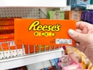 a hand holding a box of Reese's Pieces in a store