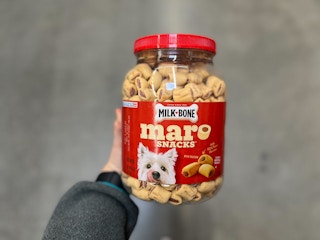 A hand holding a container of Milk-Bone MaroSnacks in a store aisle.
