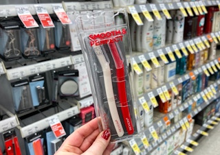 A hand holding Revlon dermaplaning razors in a store aisle