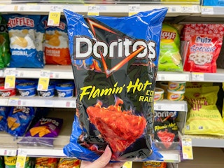 hand holding up bag of Doritos in front of a grocery store aisle