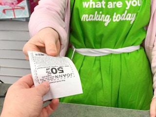 A JoAnn employee handing a coupon to a customer over the checkout counter