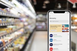 the uber eats grocery app open on an iphone in front of a blurred supermarket background