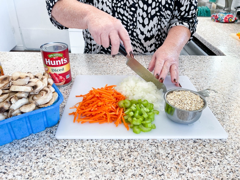 A woman preparing ingredients, chopping vegetables on a cutting board.