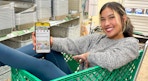 a woman sitting in a dollar tree cart holding a ihpone with the krazy coupon lady app in screen