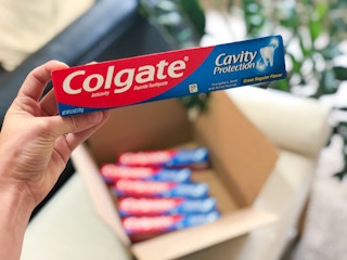 person holding colgate cavity protection toothpaste near box