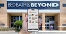 Someone holding up a phone displaying the Overstock app in front of a Bed Bath & Beyond store