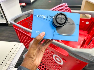 A hand holding an Echo Dot above a shopping cart.