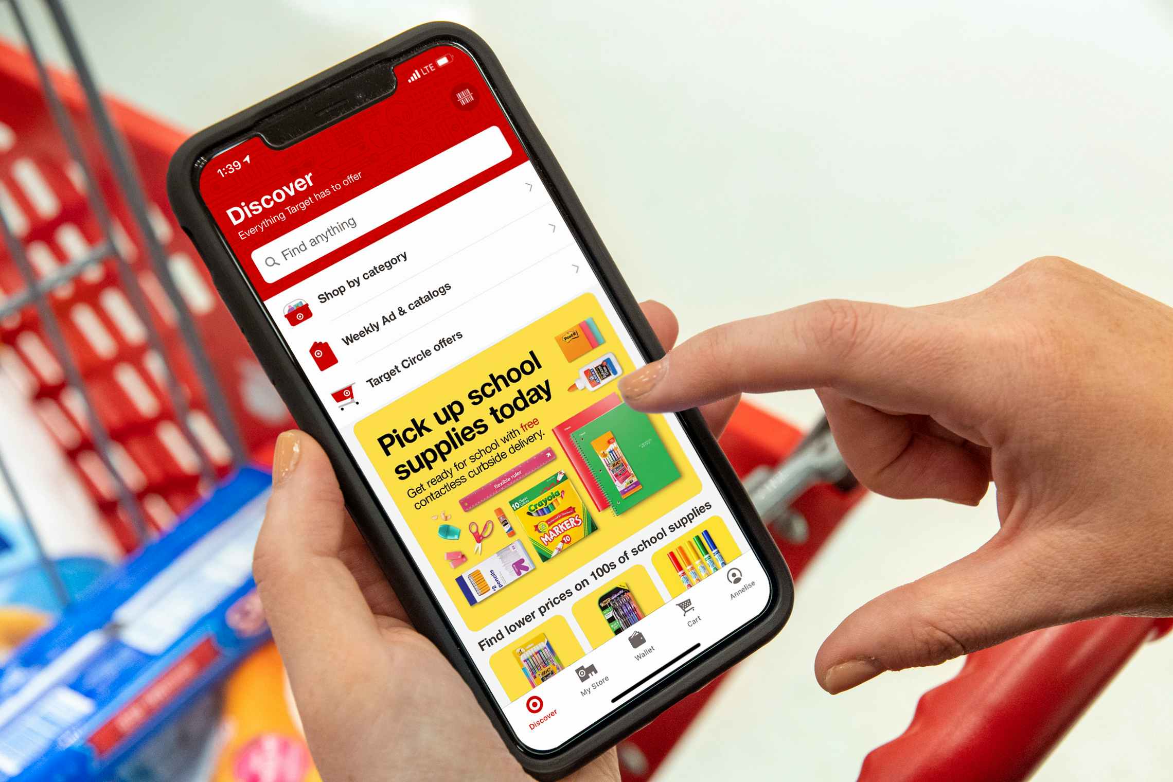 A person's hands holding a phone above a Target shopping cart with the Target app's back to school page open on the screen.