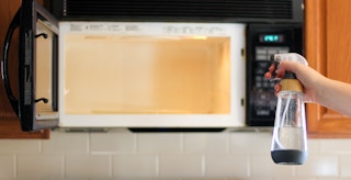 a person holding a bottle of vinegar in front of a microwave