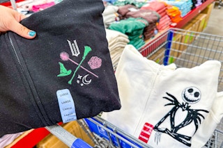 person holding a wicked themed hoodie over a sams club cart with a nightmare before christmas hoodie in it