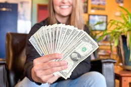 a woman sitting down and smiling holding a handful of cash fanned out 