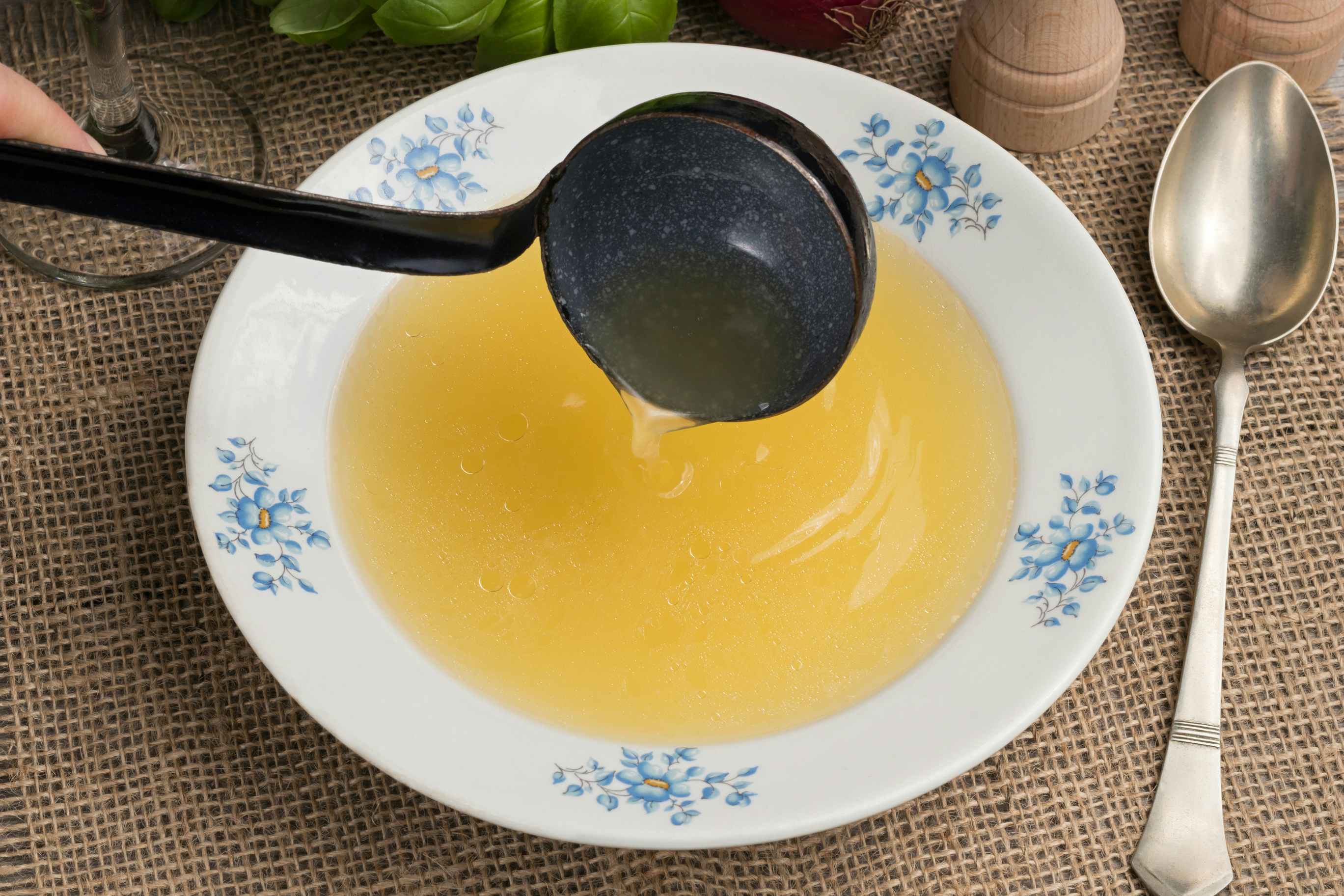 Someone pouring chicken bone broth into a soup plate with a ladle