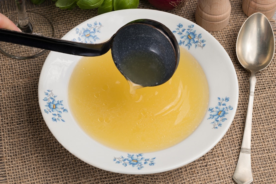 Someone pouring chicken bone broth into a soup plate with a ladle