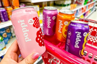 hand holding a poppi soda in front of 3 cans on a target cart