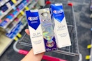 person holding 3 crest premium toothpastes over a cart