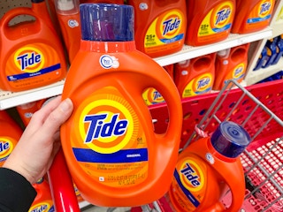 A hand holding Tide liquid laundry detergent in a store aisle.