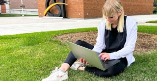 college student sitting on the grass looking at laptop
