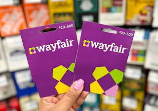 hand holding two Wayfair gift cards in front of gift card display