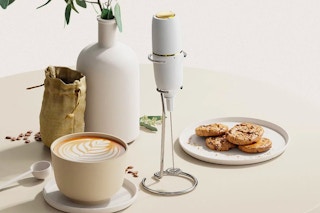 The milk frother on a table with cookies, decor, and a cup of coffee