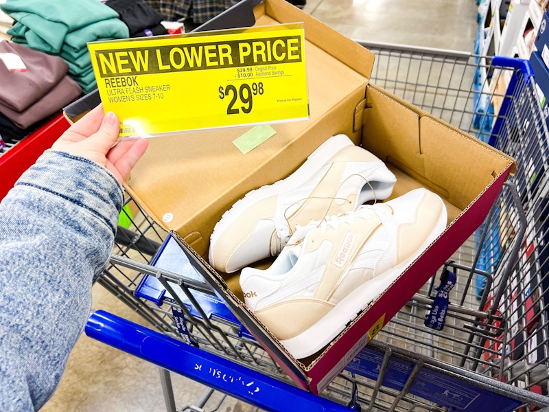 person holding a $29.98 sign by a pair of reebok womens sneakers