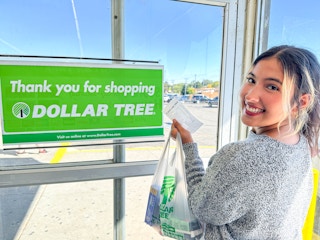 a woman smiling holding her dollar tree bag and receipt in store 