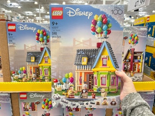 a person holding up a box of lego disney up house