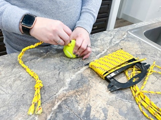 a person cutting a tennis ball next to rope to make a diy dog toy 