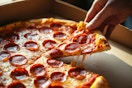 a hand grabbing a pepperoni pizza out of a pizza hut box