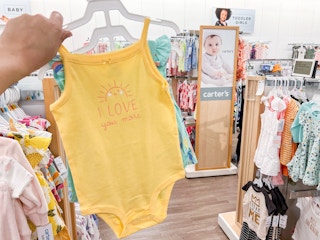 a hand holding up a carter's three piece set in the baby clothing area at kohl's