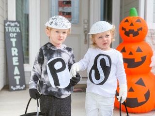Two kids in salt and pepper costumes holding hands on the porch in front of some Halloween decorations.