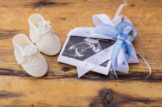 Baby boots and a sonogram photo with a bow on it sitting on a wooden table.