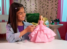 a little girl playing with a doll that has on a pink dress