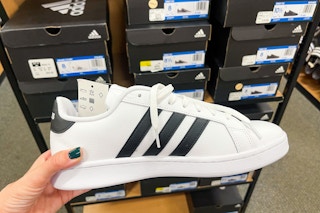 An Adidas Grand Court Mens Sneaker held out in front of several boxes of Adidas.