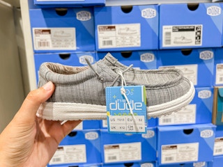 a hand holding up a kids hey dude shoe in DSW