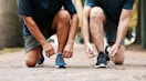 Two people tying their shoes at the same time on a walk path