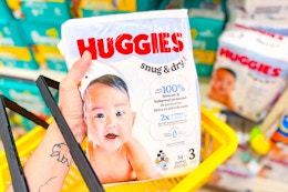 hand holding huggies diapers in a yellow shopping basket