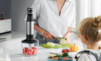 a person chopping food next to an immersion blender on a counter